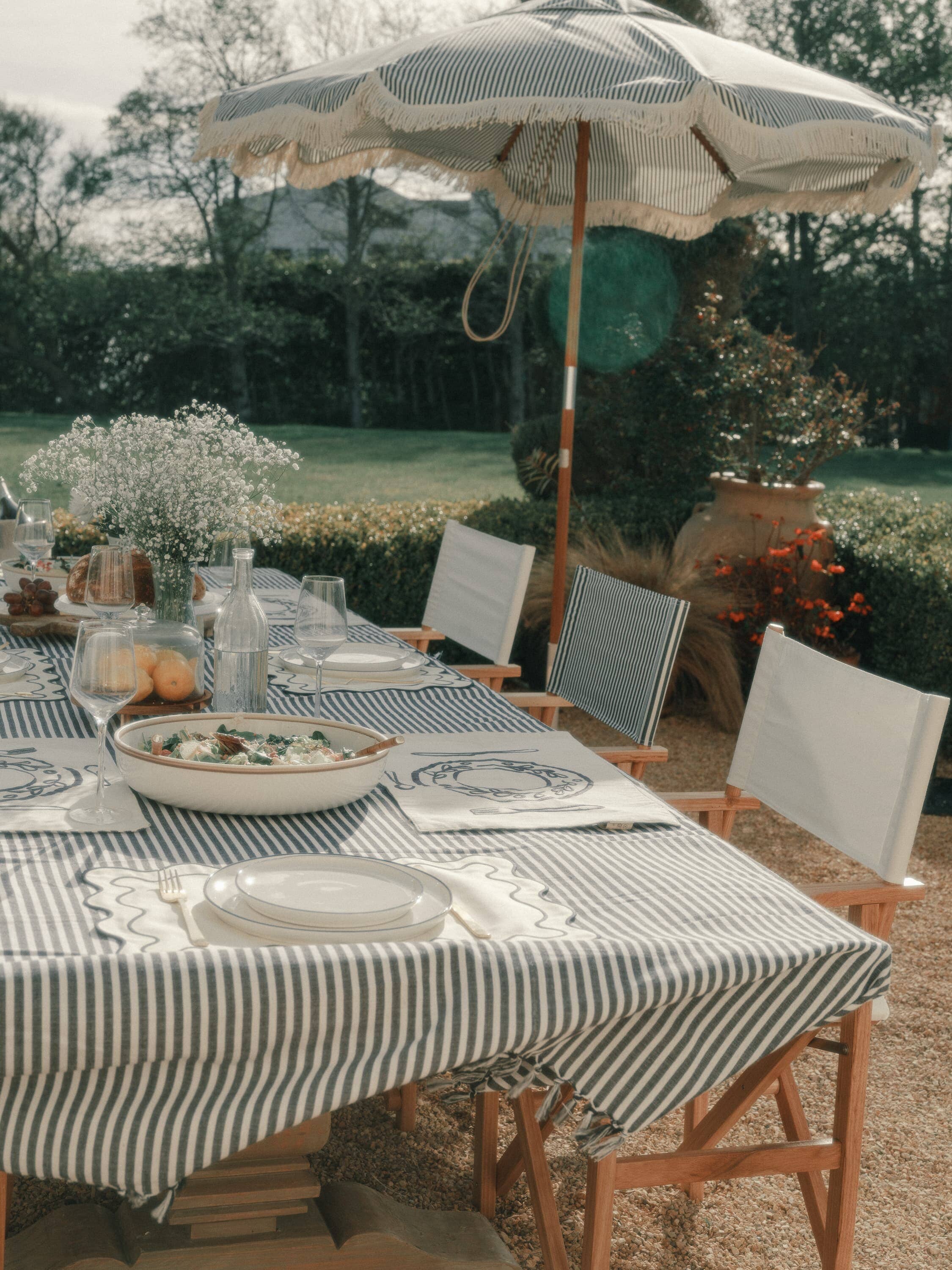 Al fresco dining table with navy stripe table cloth, directors chairs and market umbrella