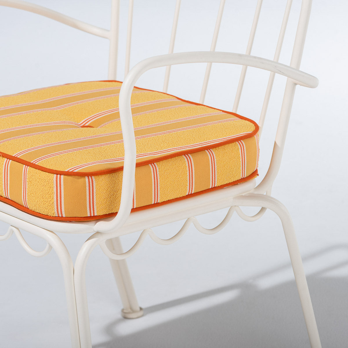 A close-up of a striped cushion on a white metal patio chair against a light gray background.