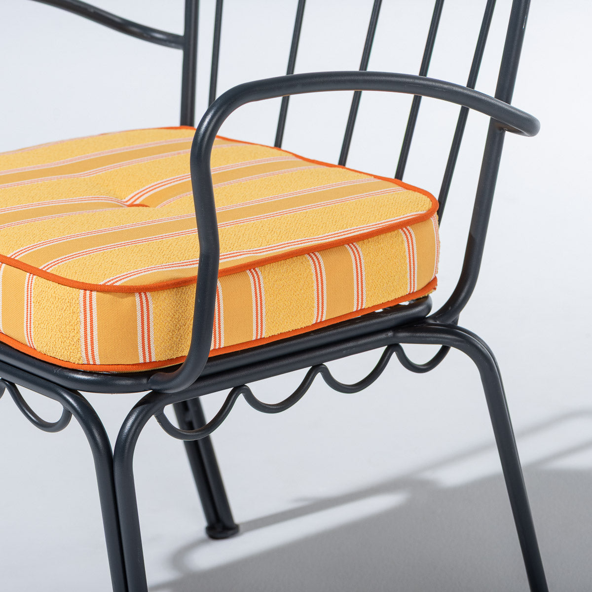 A close-up of a black metal patio chair with a thick, square yellow cushion featuring orange and white stripes.